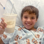 benjamin holds a milkshake. he is smiling an in a hospital bed