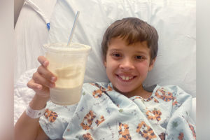 benjamin holds a milkshake. he is smiling an in a hospital bed