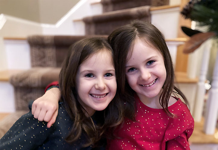 Macy and her twin sister, Isabel, sit next to each other on stairs. They have their arms wrapped around each other. 
