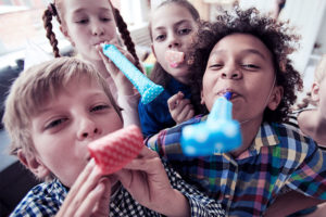 Four children blowing paper horns in celebration.