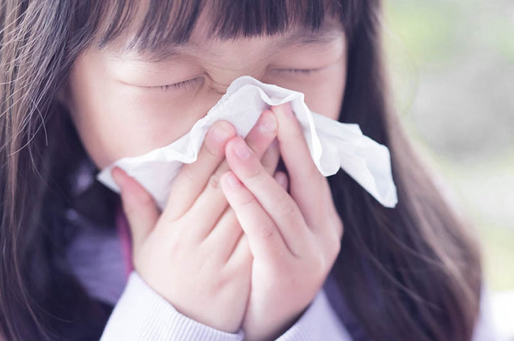 A girls sneezes into a tissue.
