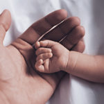 An adult hand holding an infant's hand