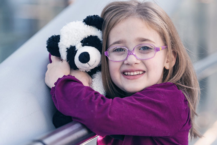 Addison holds her stuffed panda bear. She is wearing glasses.