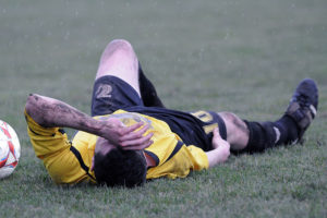 Injured soccer player lays on the field. Clavicle fracture is a common sports injury.