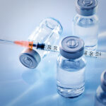 In a photo illustration, a syringe sits on top of a vial lying on its side, among other vials.