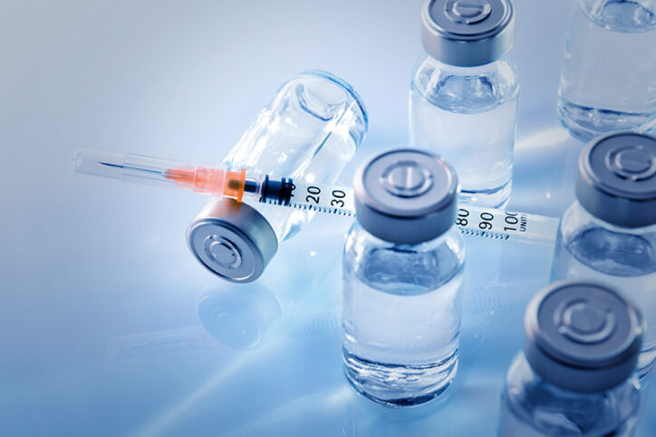In a photo illustration, a syringe sits on top of a vial lying on its side, among other vials.