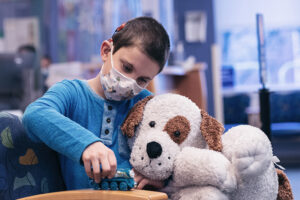 A young boy holds a large stuffed dog while playing with a toy train.