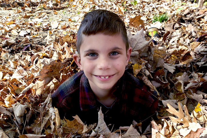 Caleb, who has a cochlear implant, plays outside in a pile of leaves.