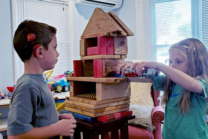 Caleb, who has a cochlear implant, builds train tracks with his sister at home.