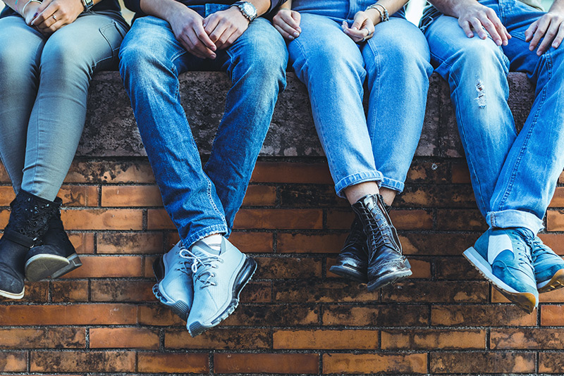 The legs and feet of teenagers dangle over a brick wall they're sitting on.