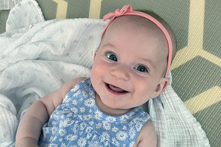 A smiling baby girl with a pink bow in her hair.