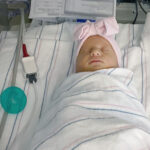 A swaddled baby girl in a NICU bassinet.
