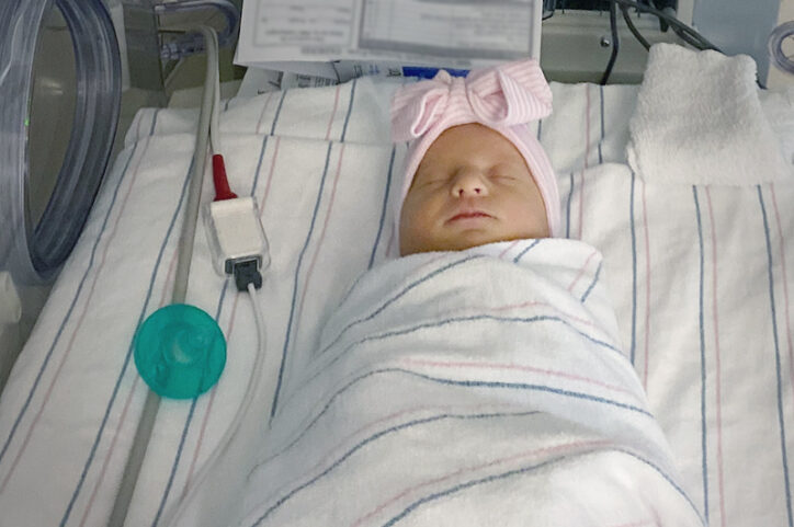A swaddled baby girl in a NICU bassinet.