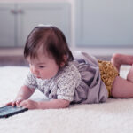 A baby alone on its tummy playing with a tablet.