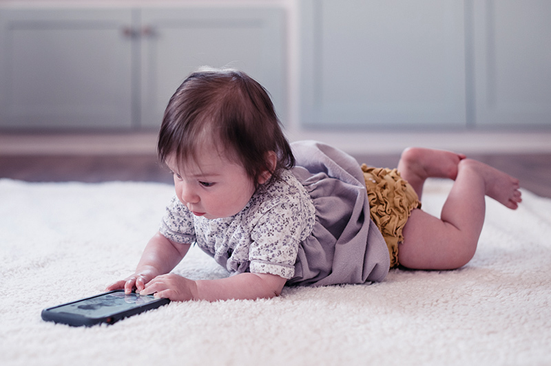 A baby alone on its tummy playing with a tablet.