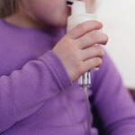 A child holds a nebulizer to her mouth.