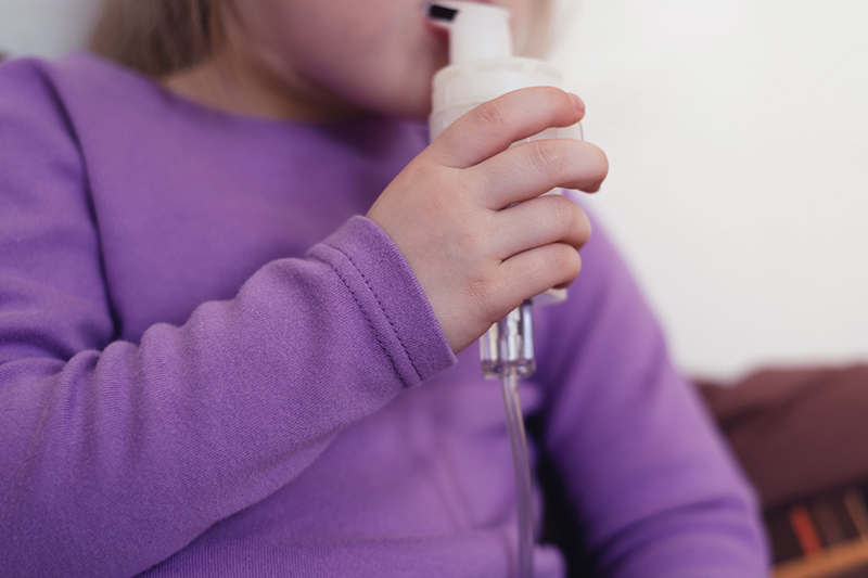 A child holds a nebulizer to her mouth.