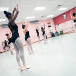 Dancers practice in a studio with a large mirror.