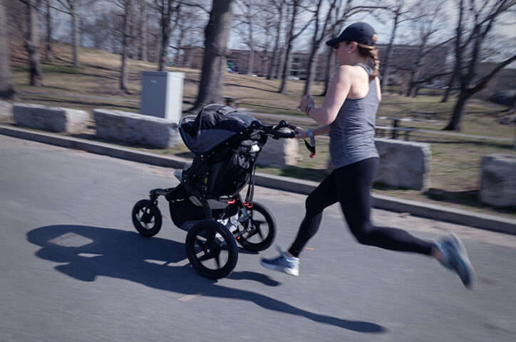 Female athlete sprints while pushing a baby stroller.