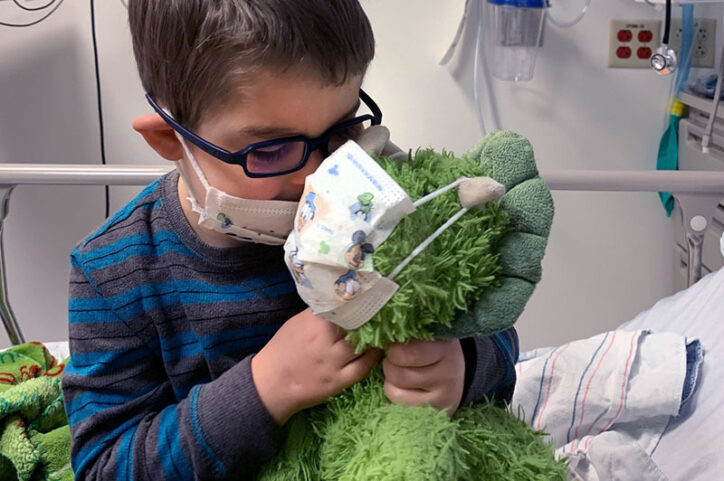 Easton sits on a hospital bed and kisses his stuffed toy, Green Animal.