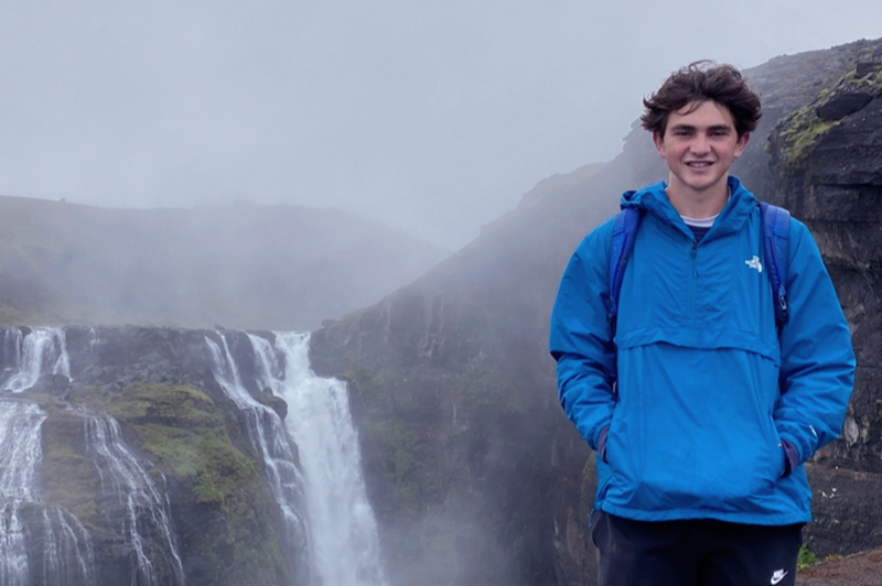 Ben stands with his hands in his pockets in front of a waterfall