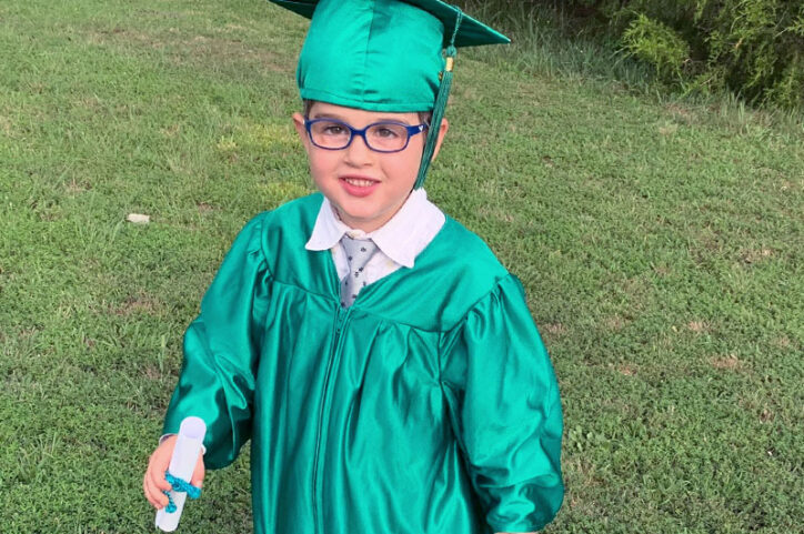 Dressed in a green cap and gown, Easton holds his kindergarten graduation diploma.