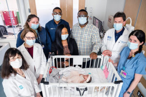 Denver in her NICU crib, surrounded by her fetal VOGM team, left to right: Dr. Carole Benson, Dr. Louise Wilkins-Haug, nurse practitioners Jennifer Judge and Christopher Isibor, Kenyatta, Derek, and Dr. Darren Orbach