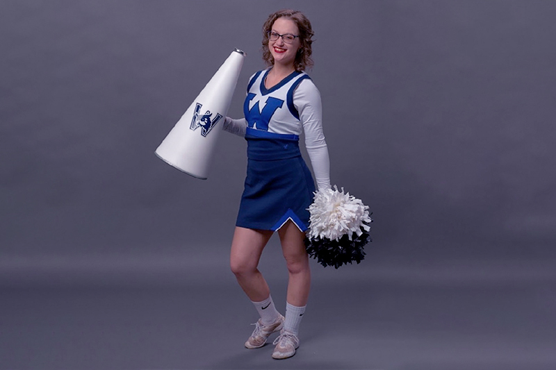 Becca Hudson in her college cheerleading costume with pompom and megaphone.