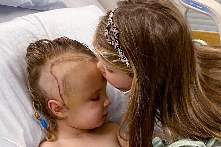 Saoirse gets a kiss on the forehead from her sister after brain surgery.