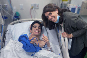 Luke, who has cerebral palsy, in a hospital bed with his mom next to him.
