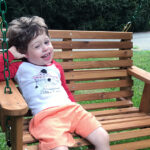 Weston, sitting here on a swing, is thriving thanks to telehealth visits