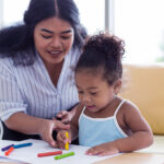 A mom helps her little girl color
