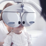 A young girl looks into a phoropter, an optometry device, during an exam.