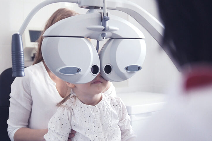 A young girl looks into a phoropter, an optometry device, during an exam.
