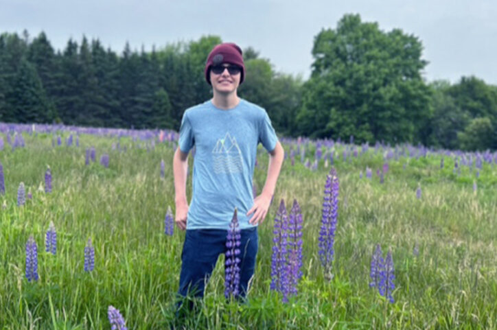 Ethan stands in a field of purple flowers in Acadia National Park after treatment for a brain tumor