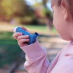 A young girl holds an asthma inhaler near her mouth.