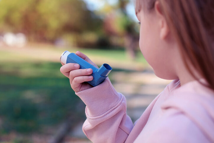 A young girl holds an asthma inhaler near her mouth.