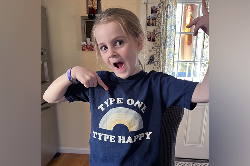 Emmie smiles and points to her shirt which reads "type one, type happy".