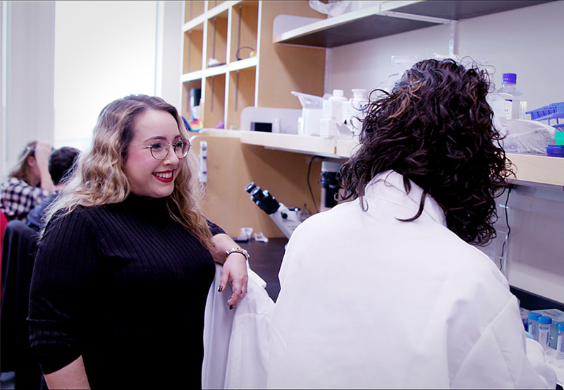 A smiling Kellie Machlus overseeing the work of a lab member.