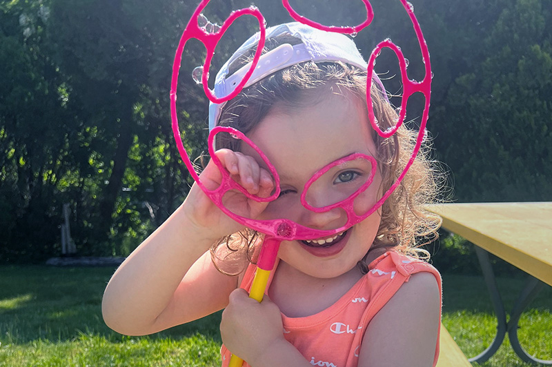 Lyla, who had retinoblastoma, holds a bubble-blowing toy as she smiles