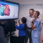 Five Boston Children's heart team members look at the image of a 3D heart model on a large wall screen.