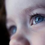 A close-up photo of top portion of a young child's face, emphasizing their eyes.