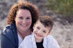 Jack and his mother sitting the sand dunes, smiling at the camera.