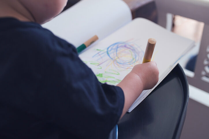 A young child with a notebook with shapes scribbled in crayon.