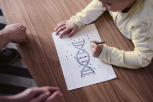 A young child connecting dots on a picture of DNA, watched by an adult.