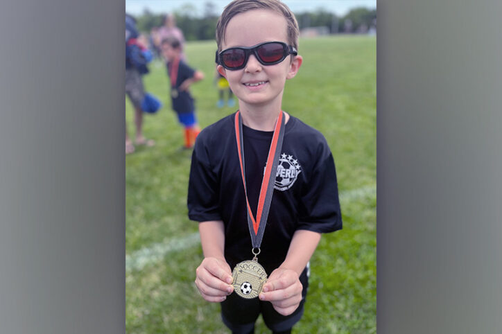 Standing on a soccer field, a young boy displays a medal he received for playing the sport.