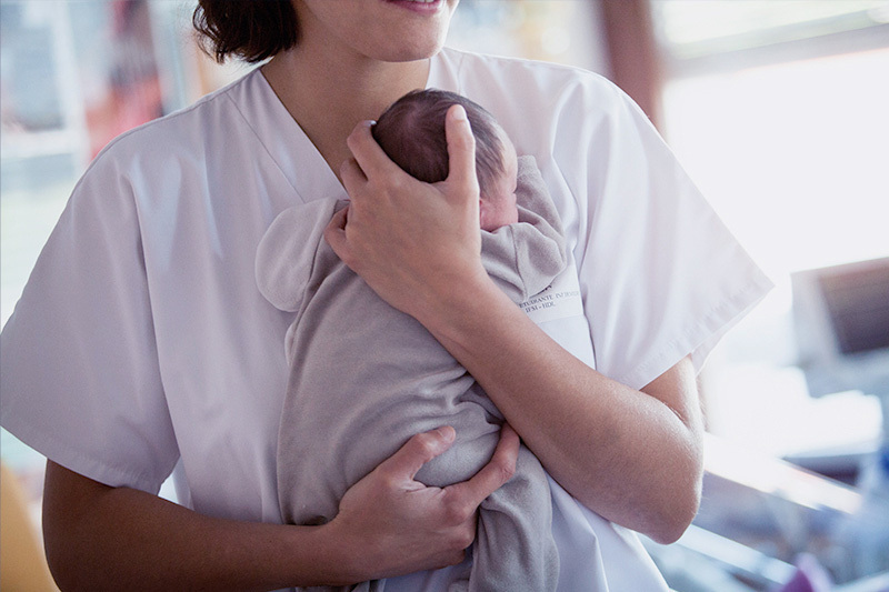 A woman holds a baby close to her chest in a hospital setting.