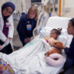 Clinicians gather at the bedside of a young patient, illustrating the concept of family-centered rounds.