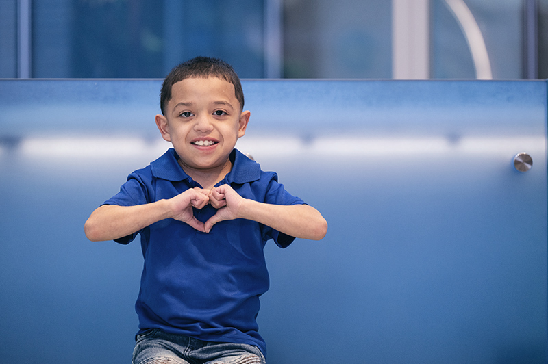 Jeremiah holds his hands in front of his chest, making a heart shape with his fingers.