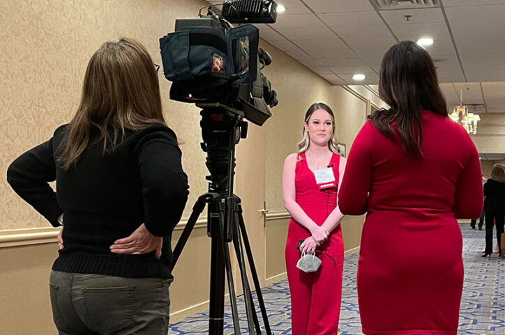 A woman is interviewed by a television news crew in a hotel conference center hallway.
